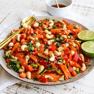 a close up of a plate of food with carrots , cashews , capsicums and limes .