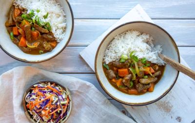 two bowls of beef curry with rice and a bowl of coleslaw on a table .