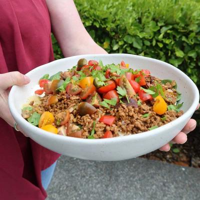 A person holds a large white bowl of mince, colourful chopped tomatoes, and fresh herbs. A person holds a large white bowl of mince, colourful chopped tomatoes, and fresh herbs.