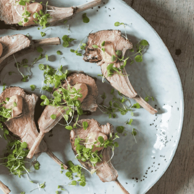 Several bone-in meat portions topped with creamy sauce and fresh microgreens on a plate.