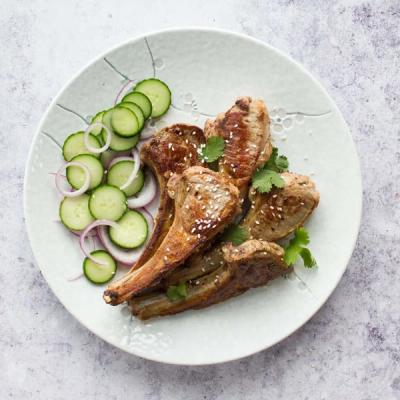 Grilled lamb chops with sesame seeds and cilantro, served with sliced cucumbers and red onion.