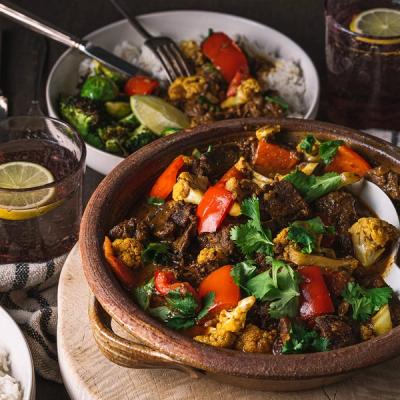 a bowl of beef stew with vegetables is sitting on a wooden table next to a bowl of rice . a bowl of beef stew with vegetables is sitting on a wooden table next to a bowl of rice .