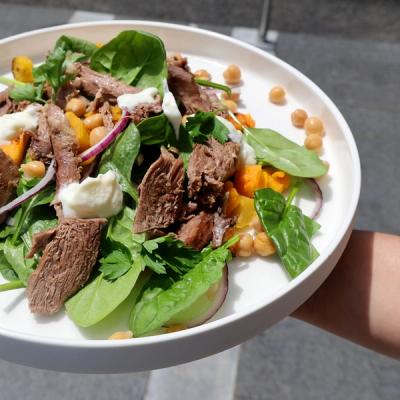 a person is holding a white plate with a salad on it topped with Harissa lamb