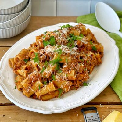 a white plate topped with pasta and meat sauce on a wooden table. a white plate topped with pasta and meat sauce on a wooden table.