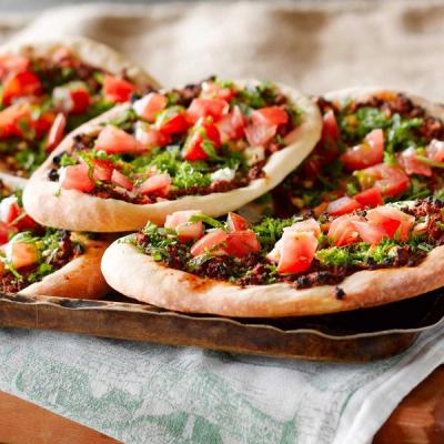 a tray of pizzas with tomatoes, lamb mince and herbs sitting on a table. a tray of pizzas with tomatoes, lamb mince and herbs sitting on a table.