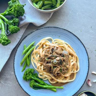 Beef stroganoff with pasta, green beans, and broccolini on a blue plate. Beef stroganoff with pasta, green beans, and broccolini on a blue plate.