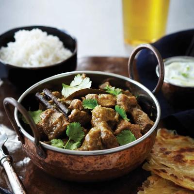 a bowl of lamb curry with rice and roti on a table .