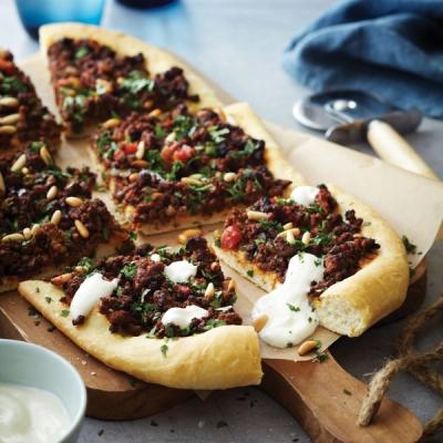 Slices of Middle Eastern-style flatbread topped with spiced ground meat, pine nuts, herbs, and yogurt sauce, on a wooden board. Slices of Middle Eastern-style flatbread topped with spiced ground meat, pine nuts, herbs, and yogurt sauce, on a wooden board.