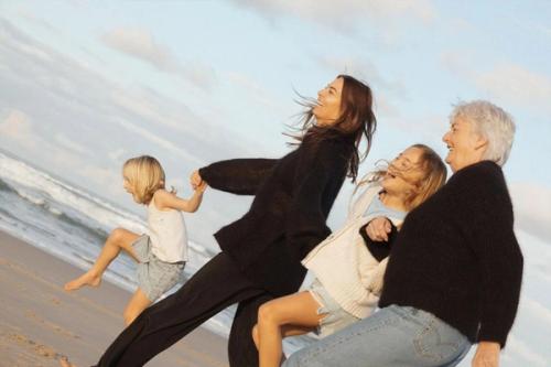 two women and two children are walking along a beach. hands . two women and two children are walking along a beach. hands .
