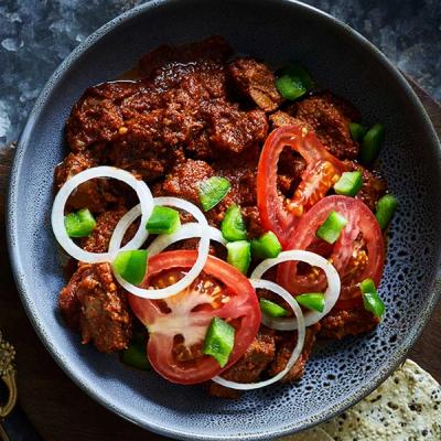 a bowl of food with tomatoes , peppers , onions and sauce on a table . a bowl of food with tomatoes , peppers , onions and sauce on a table .