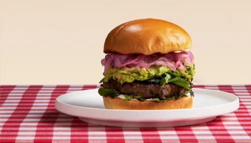 A burger with guacamole, pickled red onions, and greens, on a white plate and red checkered tablecloth. A burger with guacamole, pickled red onions, and greens, on a white plate and red checkered tablecloth.