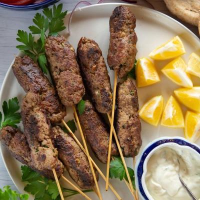 Grilled meat kebabs on skewers with lemon wedges and a bowl of tzatziki sauce. Grilled meat kebabs on skewers with lemon wedges and a bowl of tzatziki sauce.