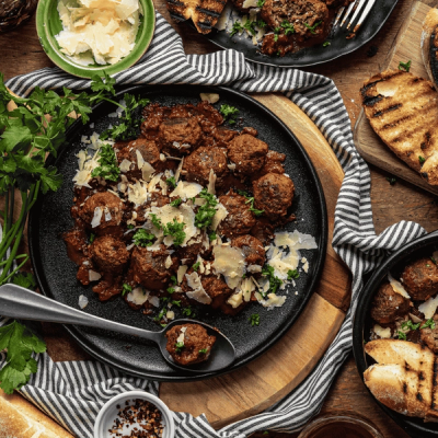 Overhead view of meatballs in sauce, garnished with grated cheese and parsley, served with grilled bread. Overhead view of meatballs in sauce, garnished with grated cheese and parsley, served with grilled bread.
