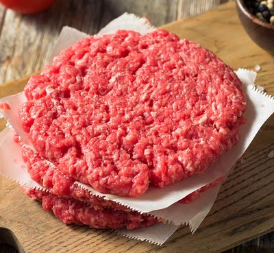 three raw hamburger patties are stacked on top of each other on a wooden cutting board . three raw hamburger patties are stacked on top of each other on a wooden cutting board .