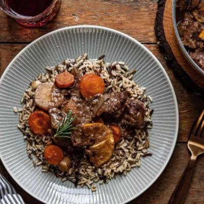 A plate of rich stew with chunks of meat and carrots on a bed of wild rice blend, garnished with rosemary and an orange slice. A plate of rich stew with chunks of meat and carrots on a bed of wild rice blend, garnished with rosemary and an orange slice.