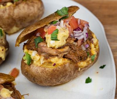 a white plate topped with stuffed potatoes filled with meat and vegetables . a white plate topped with stuffed potatoes filled with meat and vegetables .