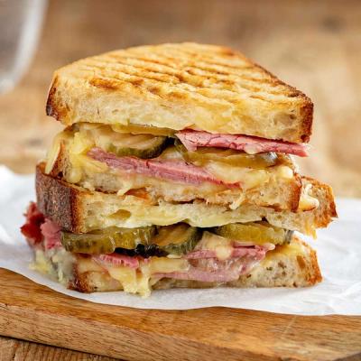 A grilled reuben sandwich, cut in half and stacked, showing corned beef, melted cheese, and pickles on a wooden board. A grilled reuben sandwich, cut in half and stacked, showing corned beef, melted cheese, and pickles on a wooden board.
