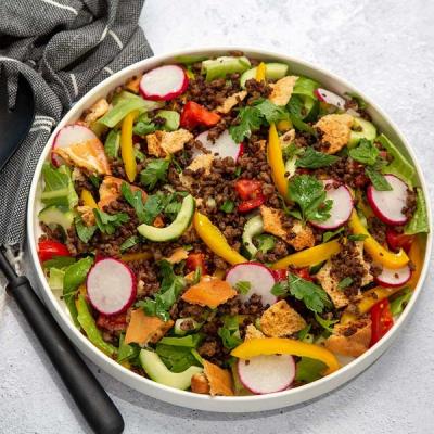 a close up of a lamb fattoush salad in a bowl with a fork. a close up of a lamb fattoush salad in a bowl with a fork.