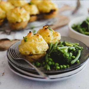a close up of a plate of food with potato top pies, broccoli and peas on a table .
