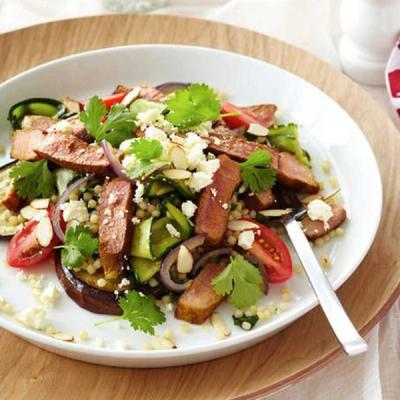 Sliced grilled lamb with couscous, mixed vegetables, feta, and coriander on a white plate. Sliced grilled lamb with couscous, mixed vegetables, feta, and coriander on a white plate.