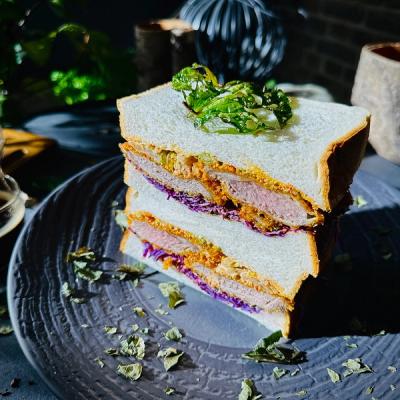 A stacked lamb sando with purple cabbage and green garnish on a dark plate.
