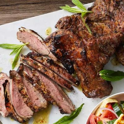 Grilled meat, partially sliced, garnished with mint leaves, with a side salad visible.