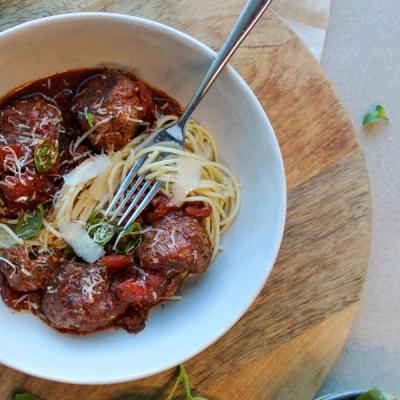 Spaghetti and meatballs in a bowl with grated cheese, fresh herbs, and a fork. Spaghetti and meatballs in a bowl with grated cheese, fresh herbs, and a fork.