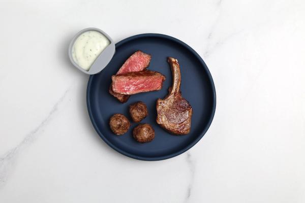 a blue plate topped with meat and potatoes next to a bowl of ranch dressing . a blue plate topped with meat and potatoes next to a bowl of ranch dressing .