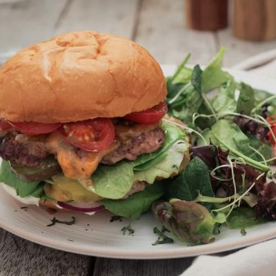 A cheeseburger topped with lettuce, tomato, pickles, and melted cheese, served with a side of mixed greens on a white plate.