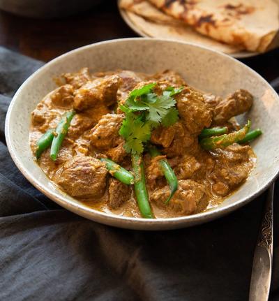a bowl of beef curry with green beans and rice on a table . a bowl of beef curry with green beans and rice on a table .