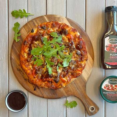 a pizza is sitting on a wooden cutting board next to a bottle of plum sauce 