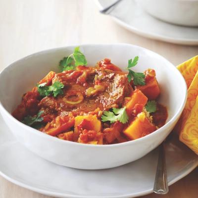 Meat and squash stew garnished with cilantro in a white bowl.