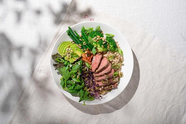 a white bowl filled with a salad , rice , broccoli , avocado and beef . a white bowl filled with a salad , rice , broccoli , avocado and beef .