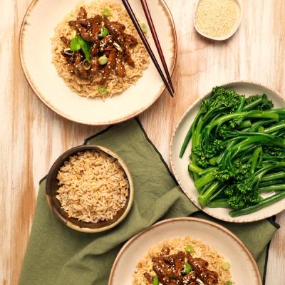 a table topped with plates of food with beef, rice , broccoli and chopsticks sitting on a plate.