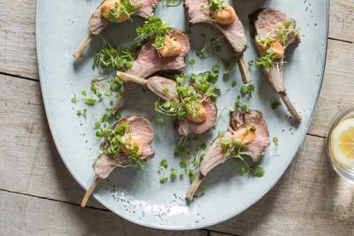 Cooked lamb cutlets garnished with sauce and microgreens on a light grey platter.