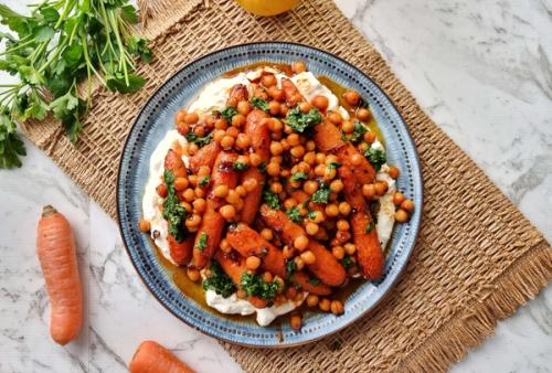 a plate of carrots and chickpeas on yogurt on a table . a plate of carrots and chickpeas on yogurt on a table .