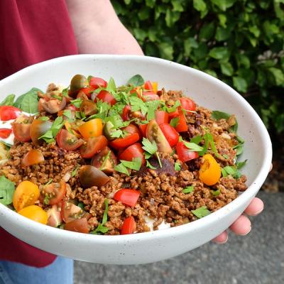 a person is holding a bowl of food with tomatoes and mince topped with coriander.