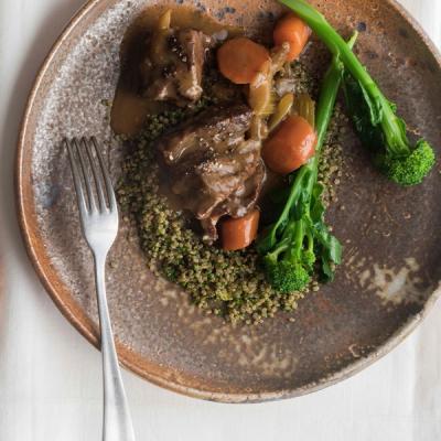 a plate of food with beef cheeks, broccoli and carrots on a table with a fork . a plate of food with beef cheeks, broccoli and carrots on a table with a fork .