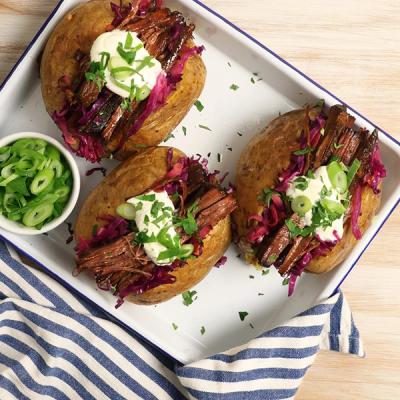 three baked potatoes filled with meat and vegetables on a tray on a table . three baked potatoes filled with meat and vegetables on a tray on a table .