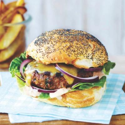 A burger on a poppy seed bun with melted cheese, lettuce, red onion, and sauce, with fries in the background. A burger on a poppy seed bun with melted cheese, lettuce, red onion, and sauce, with fries in the background.
