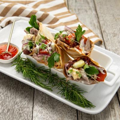 Mini wraps filled with lamb, vegetables, and sauces, garnished with rosemary, served on a white platter with chili sauce. Mini wraps filled with lamb, vegetables, and sauces, garnished with rosemary, served on a white platter with chili sauce.
