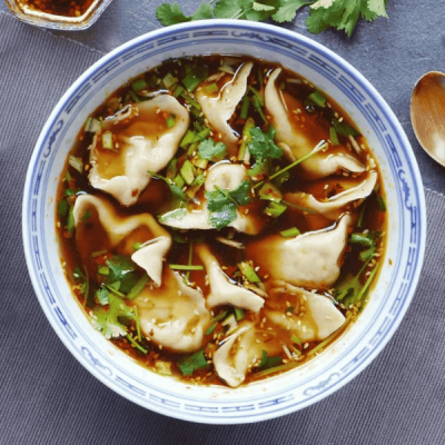 A bowl of dumplings in chili oil broth with cilantro and sesame seeds. A bowl of dumplings in chili oil broth with cilantro and sesame seeds.