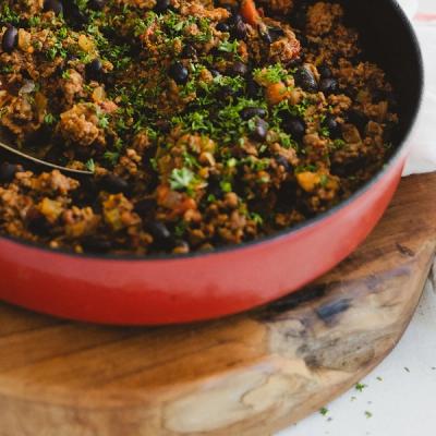 a red skillet filled with ground beef and black beans on a wooden cutting board . a red skillet filled with ground beef and black beans on a wooden cutting board .