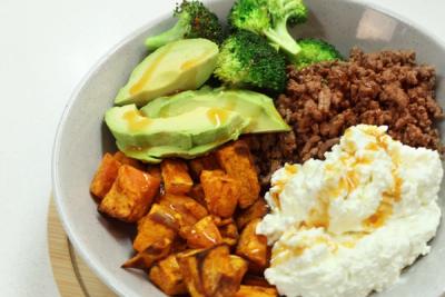 A bowl of ground beef, broccoli, sliced avocado, roasted sweet potato, and cottage cheese with a light drizzle. A bowl of ground beef, broccoli, sliced avocado, roasted sweet potato, and cottage cheese with a light drizzle.