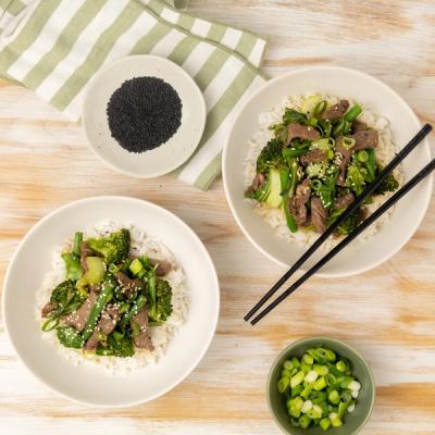 Two bowls of beef and broccoli stir-fry over white rice, topped with sesame seeds and green onions, with chopsticks resting in one bowl. Two bowls of beef and broccoli stir-fry over white rice, topped with sesame seeds and green onions, with chopsticks resting in one bowl.