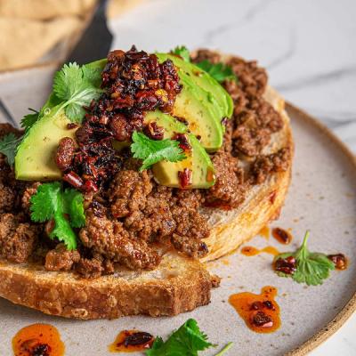 a close up of a piece of toast with avocado and mince and coriander on a plate .