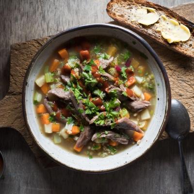 A bowl of hearty meat and vegetable barley soup, garnished with parsley and red sauce, served with buttered toast. A bowl of hearty meat and vegetable barley soup, garnished with parsley and red sauce, served with buttered toast.