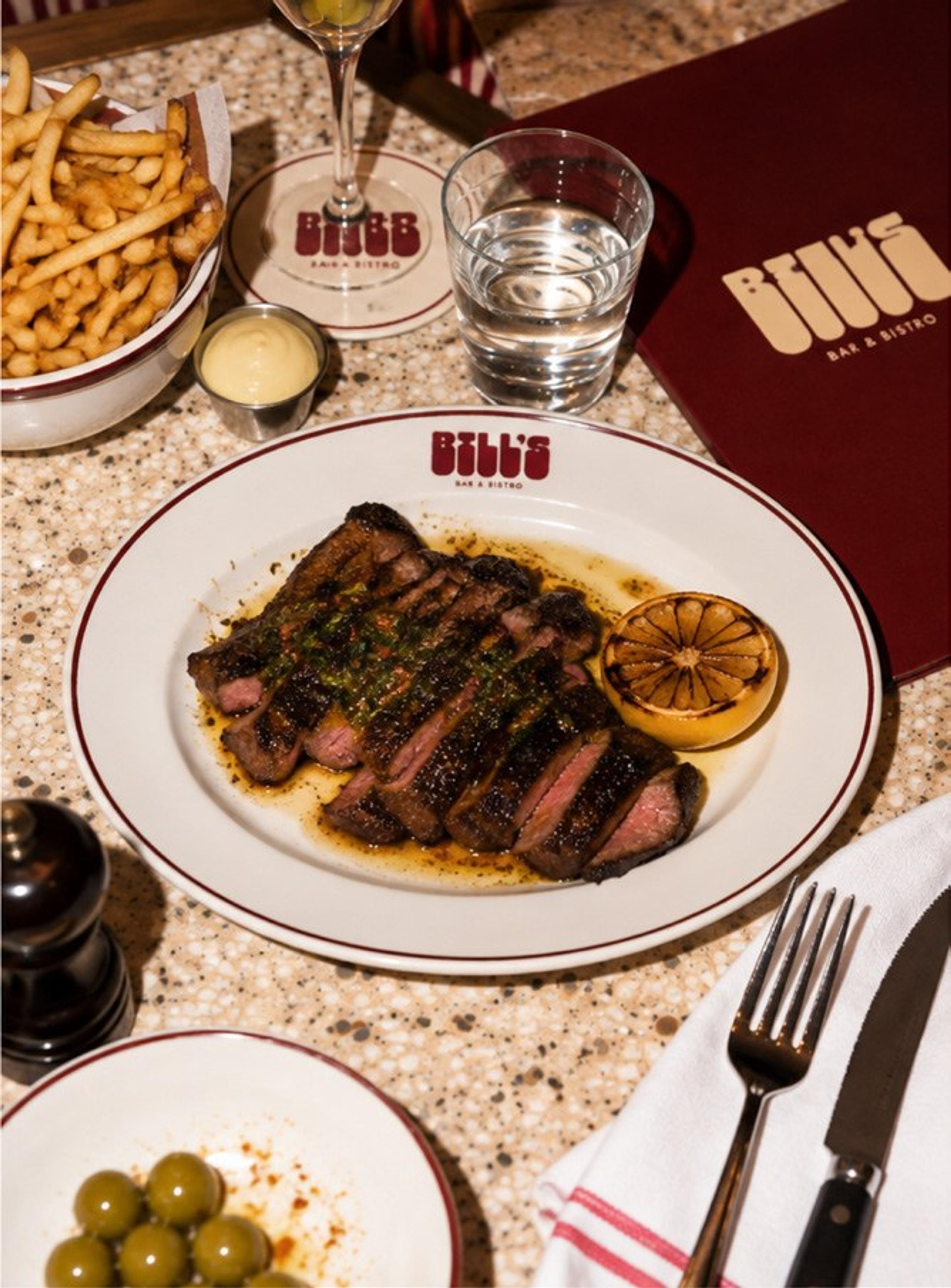 Sliced sirloin with a chargrilled lemon on a Bill’s plate, with chips and olives