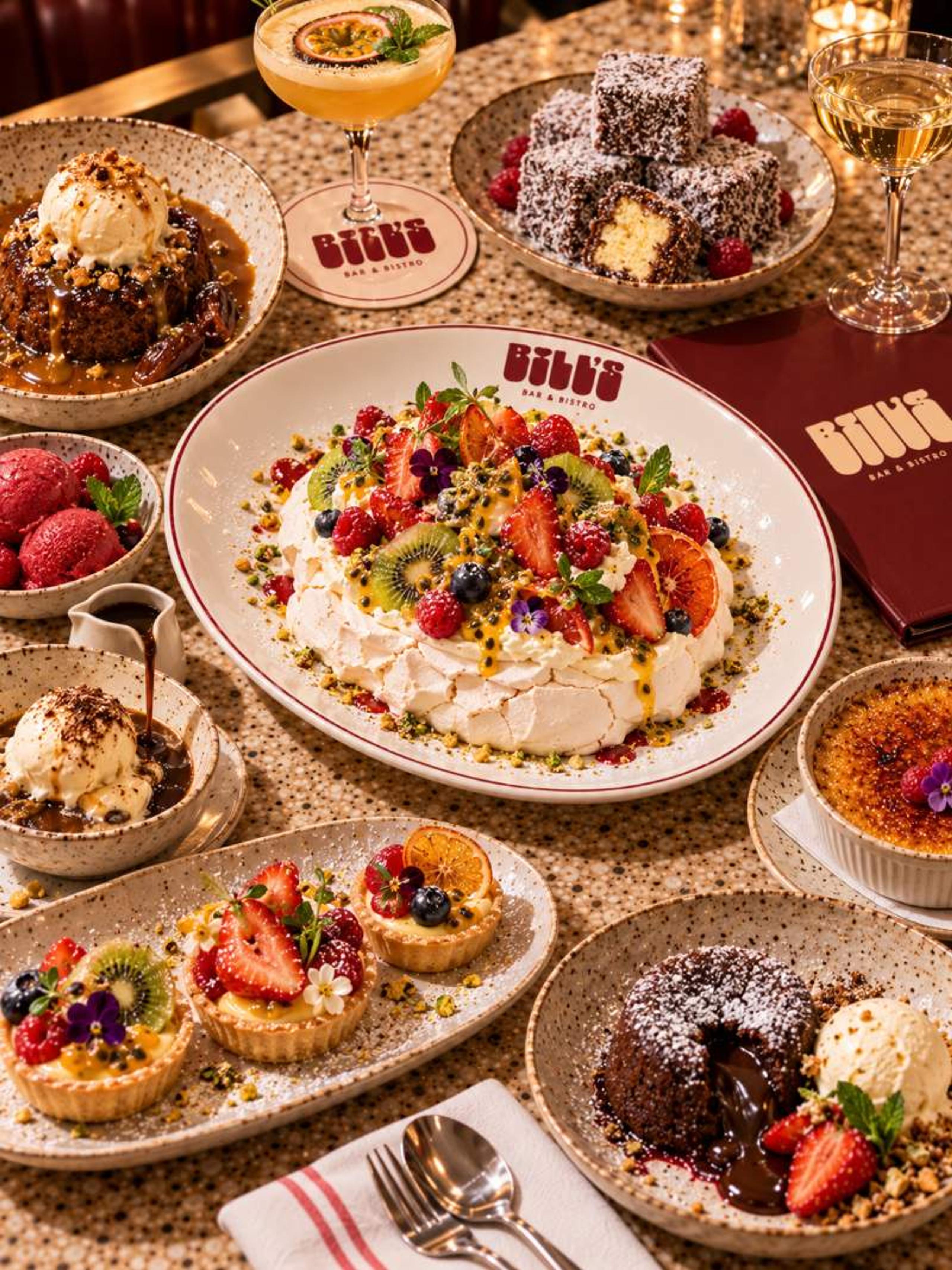 A fruit-topped pavlova on a Bill’s plate, surrounded by desserts on a terrazzo table
