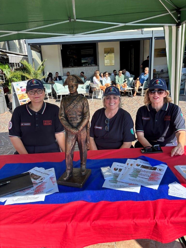 Volontarie dell'ANC Nucleo Città di Salò al tavolo informativo del gazebo con la statuetta del Carabiniere e il materiale divulgativo